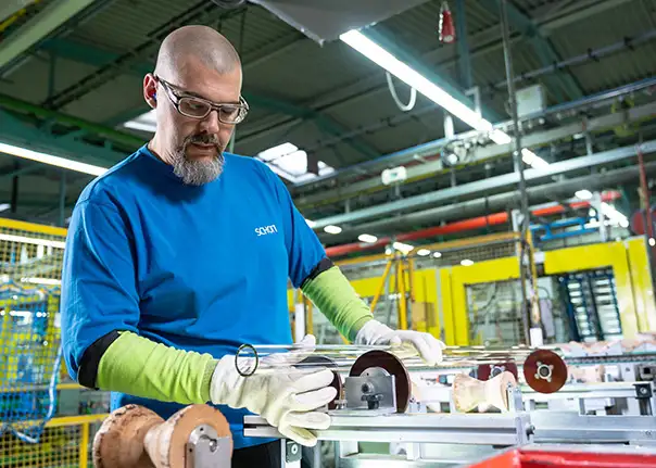 Eine Person in blauer Arbeitskleidung arbeitet an einer Produktionsanlage und richtet Glasröhren aus.