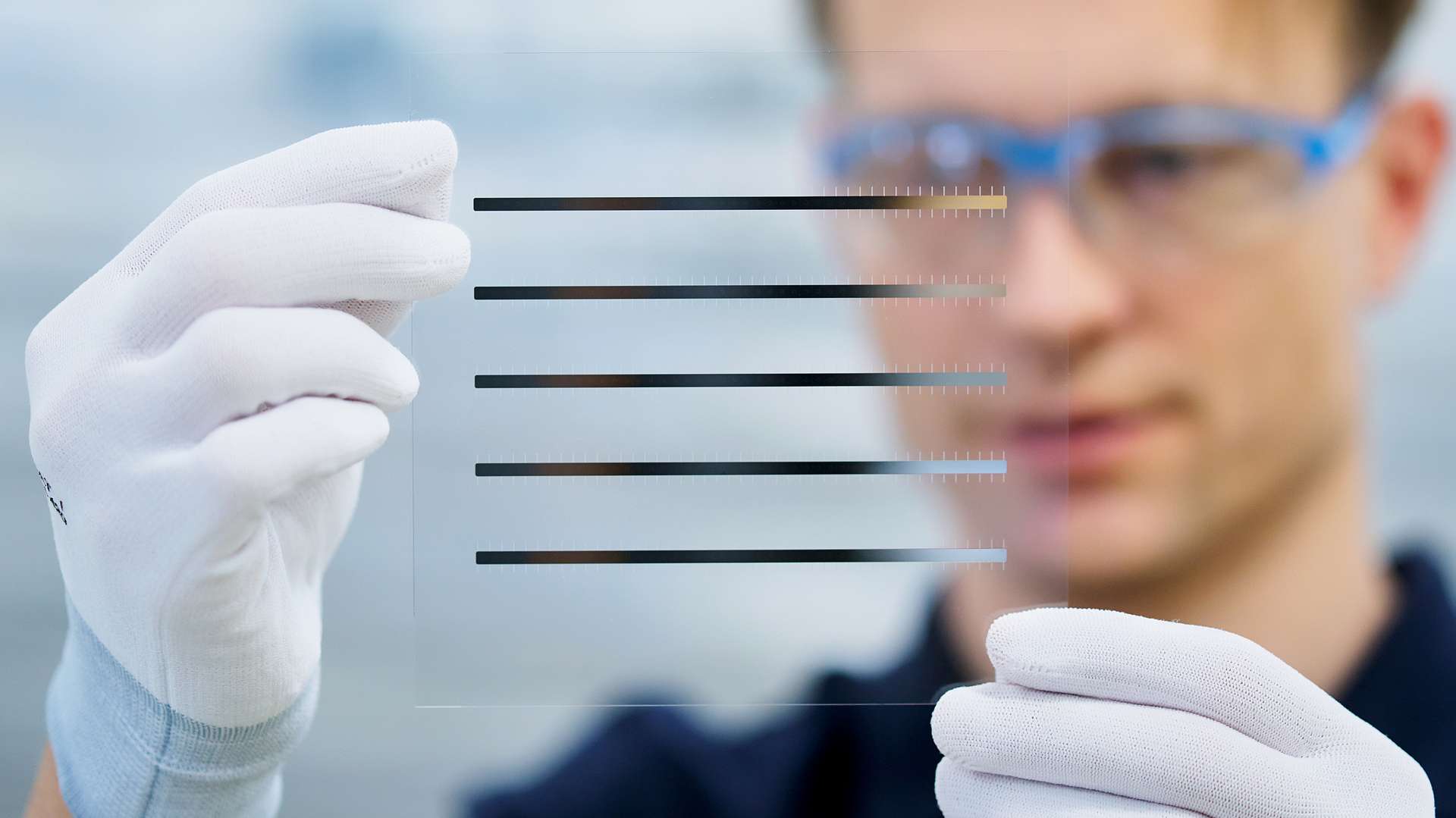 Technician inspecting a transparent glass substrate with patterned lines