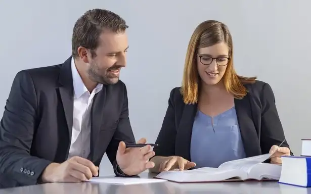 Two colleagues in a professional setting discussing and reading a document together at a desk