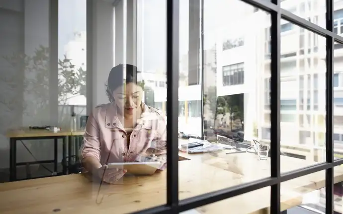 Female in an office using a tablet in front of a glass partition