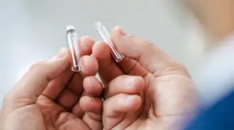 Hands holding two tiny glass containers the size of pen caps