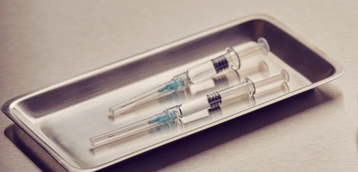 A small vial beside two syringes on a metal tray
