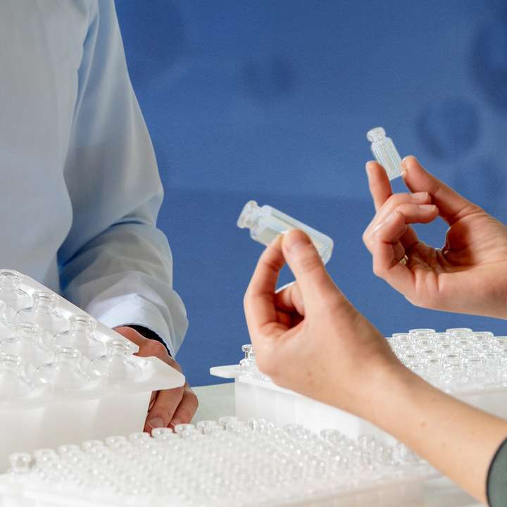 Hands holding a glass vial in front of three RTU container nests