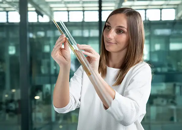 Eine Person hält zwei Glasstäbe in den Händen und beurteilt diese vor einem modernen Bürohintergrund.