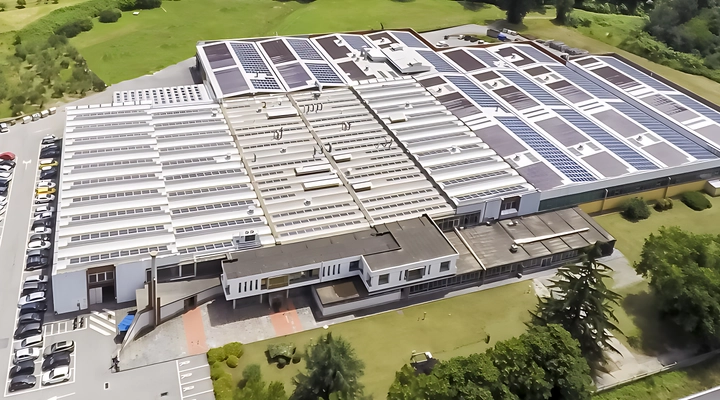 Aerial view of a large industrial manufacturing facility with multiple roof sections covered in skylights and solar panels, surrounded by greenery.