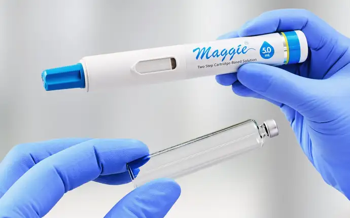 Hände mit blauen Handschuhen halten eine neue Polymerkartusche und einen großvolumigen Autoinjektoren von SHL Medical. 