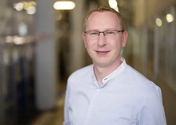 Eine Person in hellblauem Hemd steht in einem Flur einer Produktionsumgebung