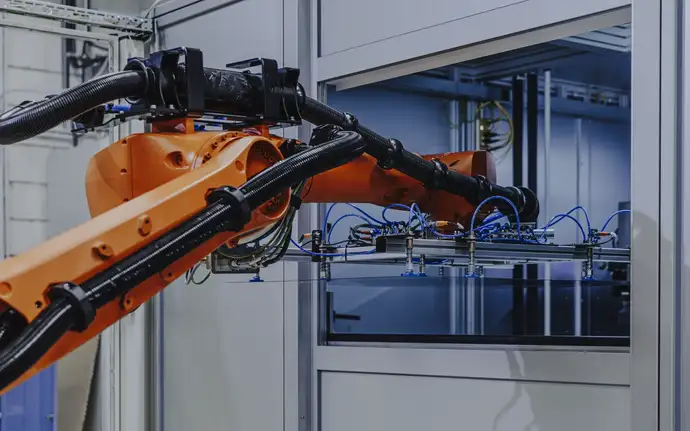 A robotic arm in an industrial setting operating near a machine enclosure.