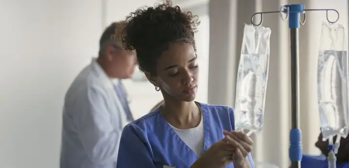 Female nurse adjusts IV equipment with clinician in background