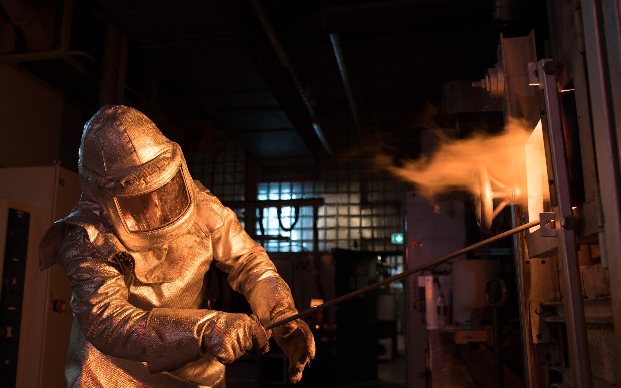 SCHOTT worker in protective clothing next to glass melting tank