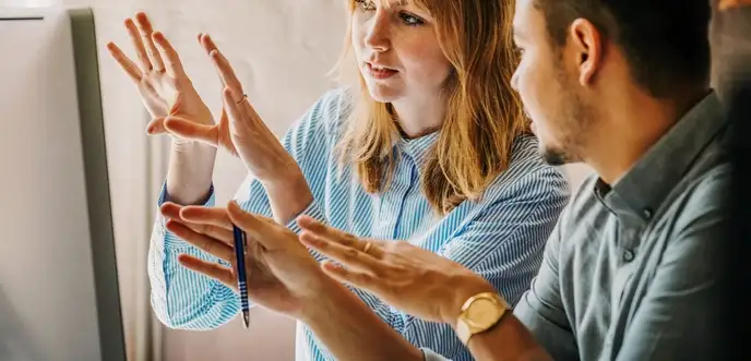 Zwei junge Menschen mit Studienabschluss arbeiten vor einem Computerbildschirm